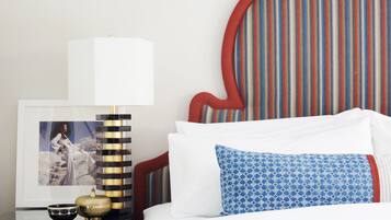 A neatly made bed with white and blue patterned pillows, a framed picture on a bedside table, and a striped wall behind.