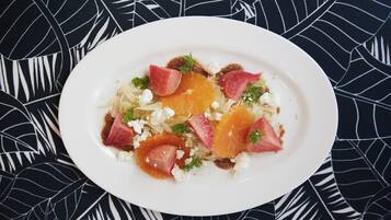 A white plate with a salad of orange segments, feta cheese, and herbs, set on a black and white leaf-patterned tablecloth.