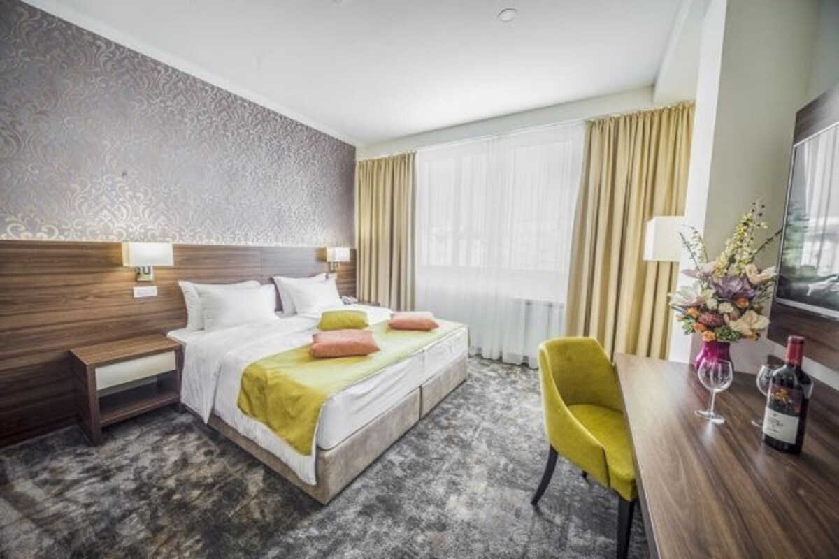 Habitación de hotel con cama, mesitas de noche, un escritorio con silla, un florero y una botella de vino.