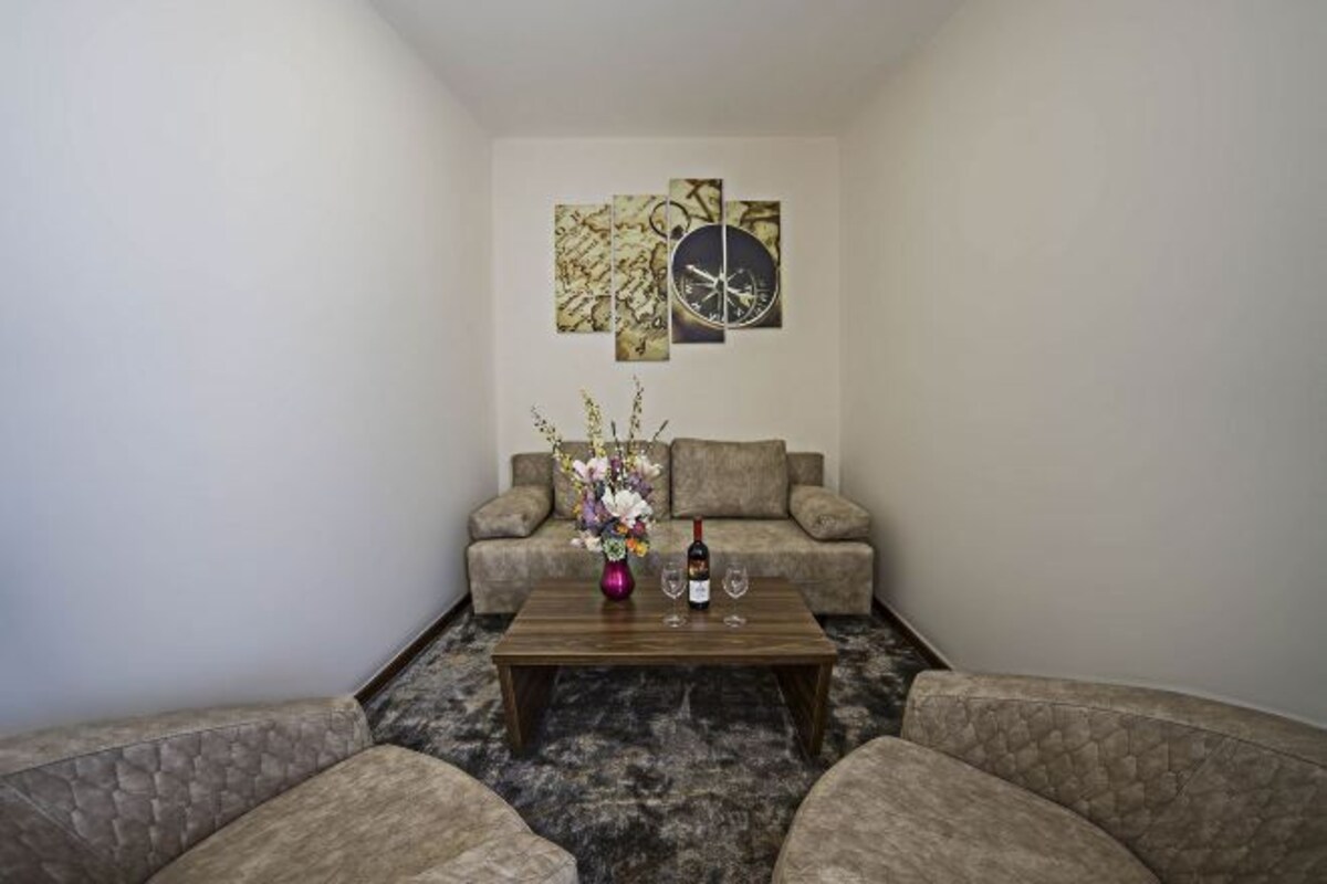 Una sala de estar con un sofá, una mesa de centro con un florero y una botella de vino, y arte abstracto en la pared.