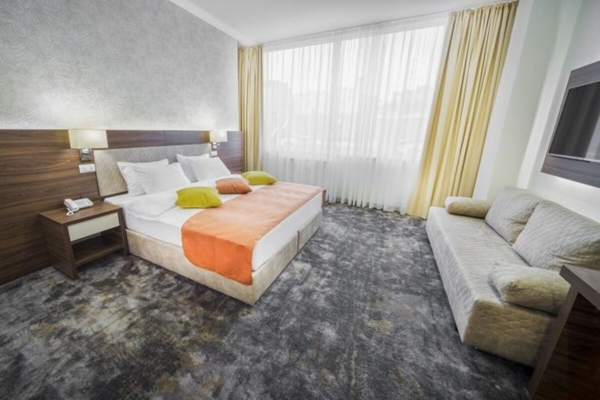 Una habitación de hotel con cama, mesita de noche, lámpara y sofá.