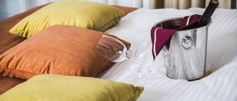 A bed with pillows, a wine glass, and a wine bottle.
