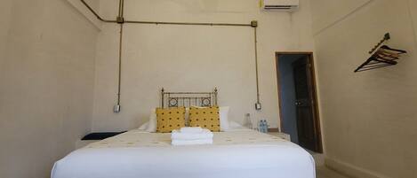 A hotel room with a bed, pillows, a bedside table with bottles, and a hanging clothes rack.