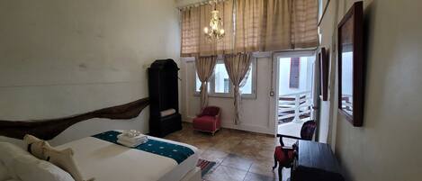 Un dormitorio con cama, armario, una silla roja, una mesa y una ventana con cortinas.