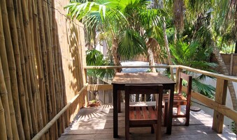 Une terrasse en bois avec une table et des chaises, entourée de murs en bambou et de plantes tropicales.