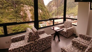 A room with large windows offering a view of a mountainous landscape. There are patterned sofas and a small table. - Golden Sunrise Machupicchu (Machu Picchu)