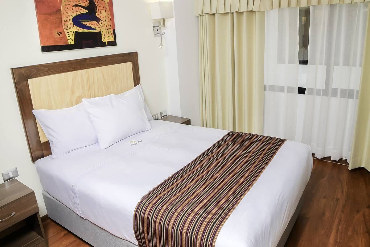 A neatly made bed with a striped blanket, a wooden headboard, and a wall-mounted lamp.