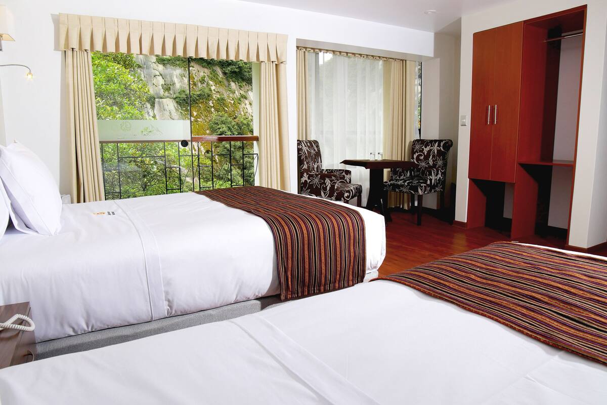 A hotel room with two beds, a desk, a chair, and a wardrobe.