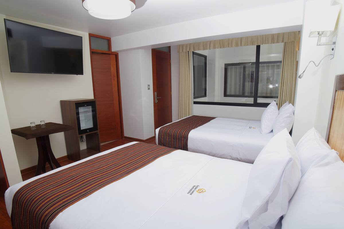 A hotel room with two beds, a TV, a desk, and a window with curtains.
