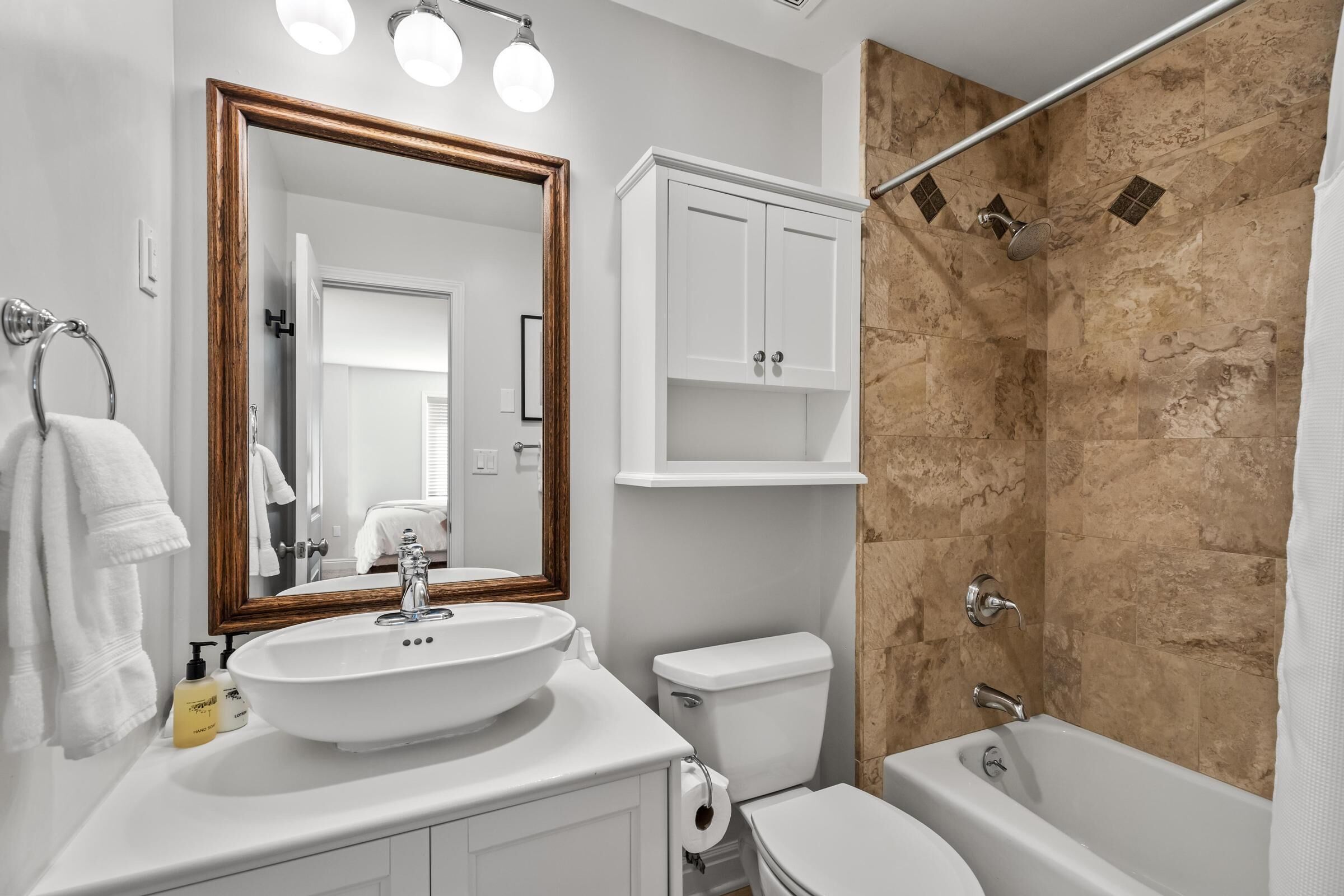 A bathroom with a white sink, a toilet, a shower with a glass door, and a mirror with a wooden frame.
