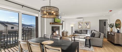 A modern living room with a dining area, large windows, and a fireplace.