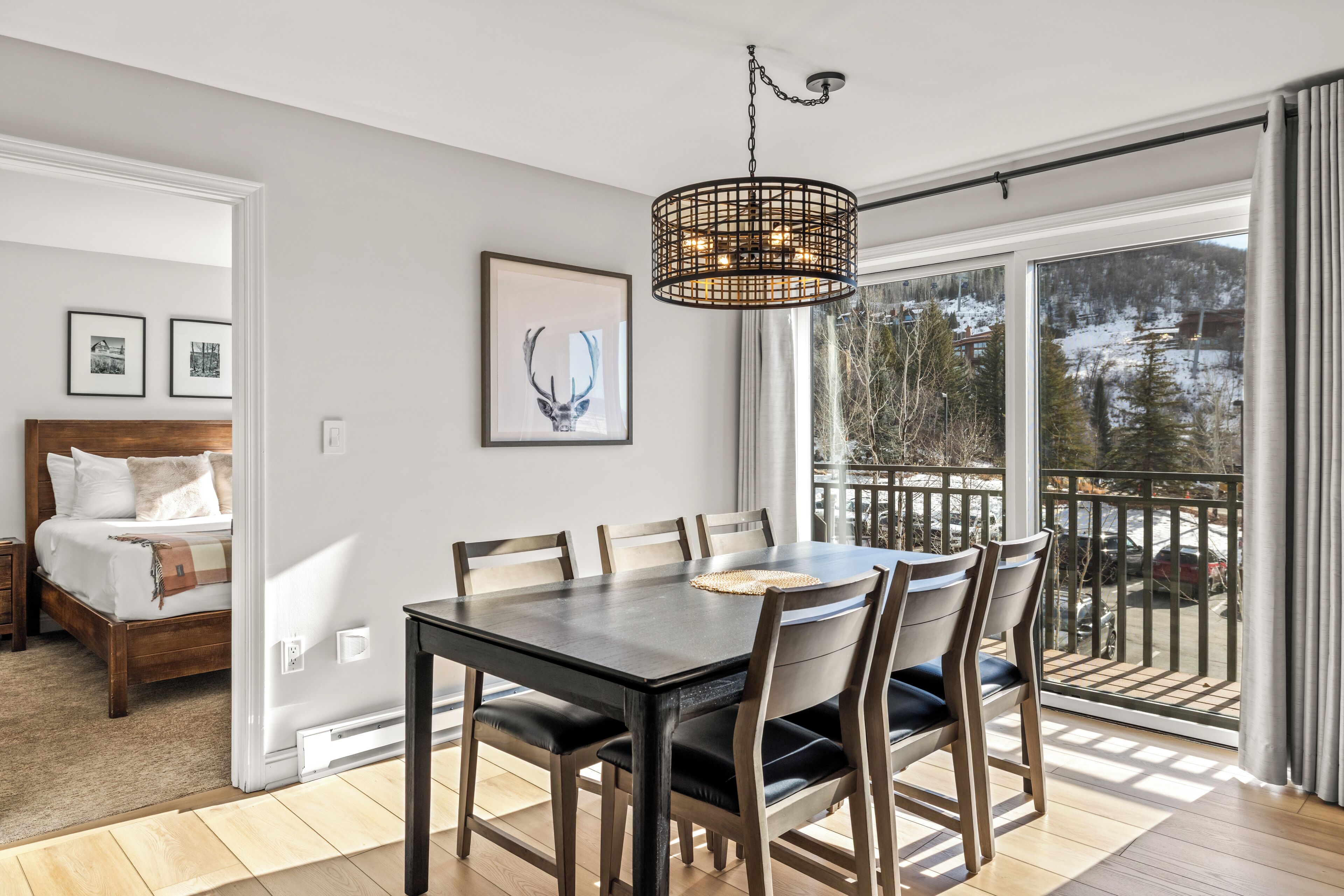 Un espace repas comprenant une table et des chaises, un lustre, et une vue sur un paysage enneigé grâce à de grandes fenêtres.