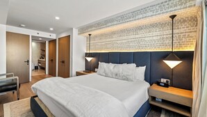 Ein modernes Hotelzimmer mit einem großen Bett, Nachttischen, einem Kopfteil mit Muster und einem sichtbaren Badezimmer im Hintergrund.