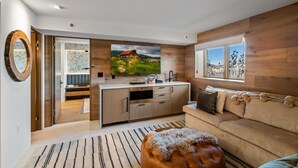 Eine moderne Küche mit großem Fernseher, Holzwänden und einer gemütlichen Sitzecke mit Sofa und Hocker.