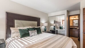 Un dormitorio bien iluminado con una cama grande, una mesita de noche, un espejo y un armario.