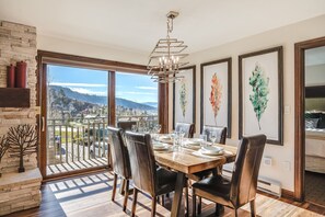 A dining area with a large table set for six, a chandelier, and framed artwork on the walls. - Bear Claw 209 Premium On Mountain Condo With Ski-In/Ski-Out Access! (Steamboat Springs)