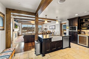 A modern kitchen with dark cabinetry, a central island, stainless steel appliances, and a view to the outside.