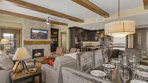A modern living room with a fireplace, grey sofas, and a dining area set for six. - Edgemont 2402 Luxury On Mountain Condo With Ski-In/Ski-Out Access! (Steamboat Springs)