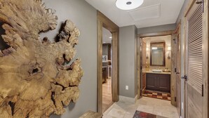 A hallway with a wooden wall art piece, a wooden bench, and a kitchen area visible through an open door. - Edgemont 2402 Luxury On Mountain Condo With Ski-In/Ski-Out Access! (Steamboat Springs)
