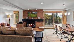 Una sala de estar con chimenea, un comedor y un ventanal con vistas a árboles.