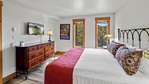 Un dormitorio con una cama grande, un aparador de madera, un televisor y una ventana con vistas a árboles.