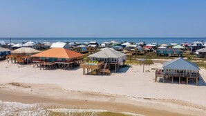 A beachfront property with multiple houses on stilts, a sandy beach, and the ocean in the background. - Family Tides | Pool, on west end. Nightly Sept stays (Dauphin Island)