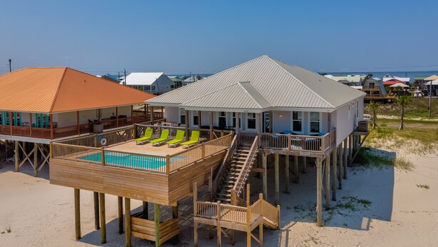A beachfront property with a wooden deck, a pool, and a staircase leading to a second floor. - Family Tides | Pool, on west end. Nightly Sept stays (Dauphin Island)