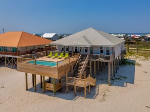 En fastighet vid stranden med en träveranda, en pool och en trappa som leder upp till ett andra våningsplan.