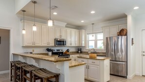 A modern kitchen with white cabinetry, stainless steel appliances, and a granite countertop. - Family Tides | Pool, on west end. Nightly Sept stays (Dauphin Island)
