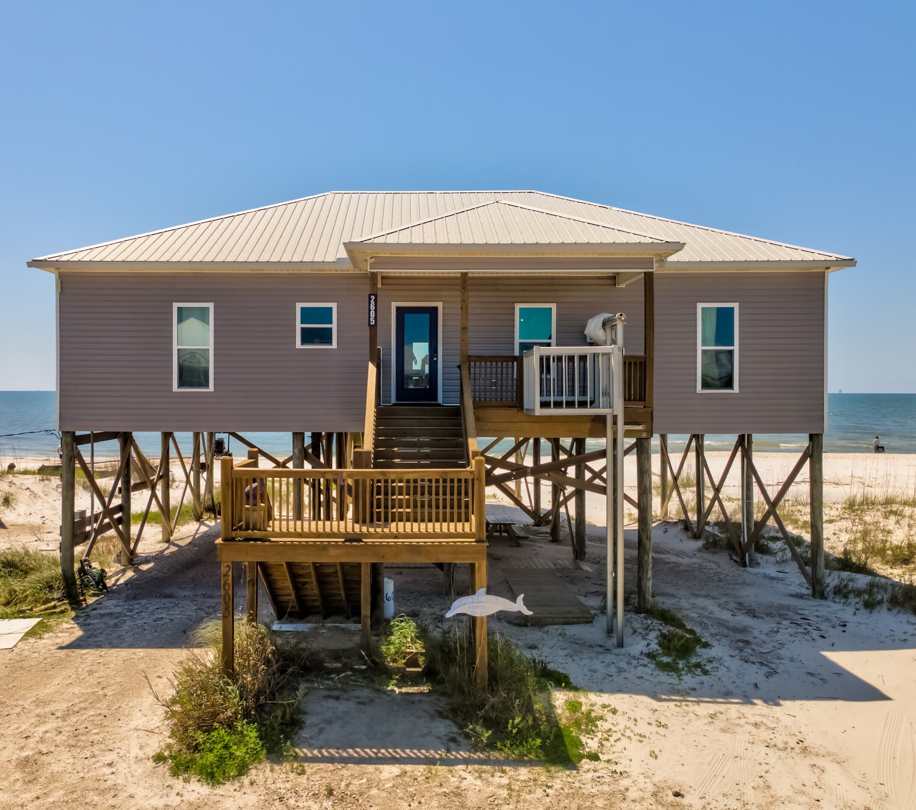 Una casa de playa con terraza de madera, puerta principal y un pequeño porche.