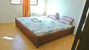 A single bed with a floral bedspread and pillows, a window with curtains, and a tiled floor. - Homestay in Dar es salaam (DSM)