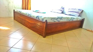 A wooden bed with a floral bedspread in a room with tiled flooring. - Homestay in Dar es salaam (DSM)