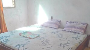 A bed with floral bedding, two pillows, and a small bedside table. - Homestay in Dar es salaam (DSM)
