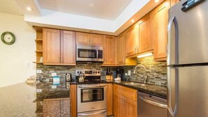A modern kitchen with wooden cabinets, stainless steel appliances, and a granite countertop. - Open Design Suite w/Modern Kitchen, Lanai to Lawn, WiFi–Kamaole Sands 9106 (KIHEI)