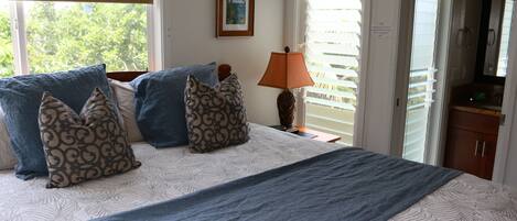 A bedroom with a bed, pillows, a lamp, and a window with blinds.