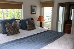 Quarto com cama, almofadas, luminária e janela com persianas.