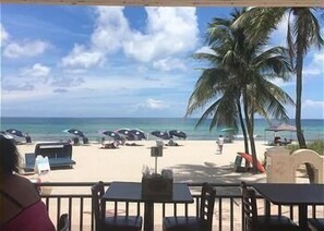 Un restaurant situé en bord de mer, avec une terrasse, une vue sur l’océan et des palmiers.