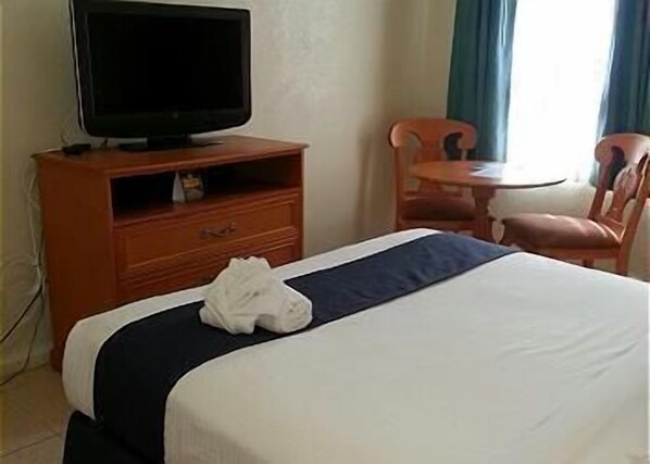 A hotel room with a bed, a television on a wooden cabinet, a small table, and two chairs.