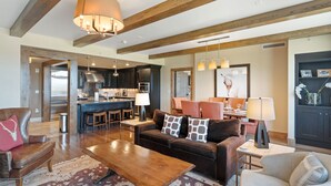 A spacious living area with a wooden ceiling, a sofa set, a coffee table, and a dining area with chairs and a lamp. - Edgemont 2703 Luxury On Mountain Condo With Ski-In/Ski-Out Access! (Steamboat Springs)