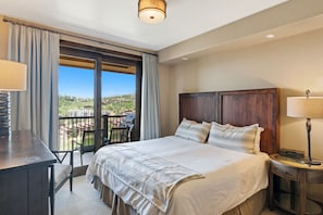 Quarto de hotel com uma cama grande, uma mesa de trabalho e uma varanda com vista para o campo.