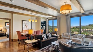 A spacious living room with a wooden ceiling, a large window offering a view of the hills, and a dining area with orange chairs and a table. - Edgemont 2703 Luxury On Mountain Condo With Ski-In/Ski-Out Access! (Steamboat Springs)