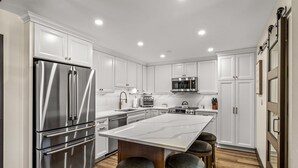 A modern kitchen with white cabinetry, stainless steel appliances, and a large island with stools.