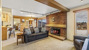 A spacious living room with a fireplace, a sofa set, a dining area, and a view of the outdoors. - Bear Claw 203 Premium On Mountain Condo With Ski-In/Ski-Out Access! (Steamboat Springs)