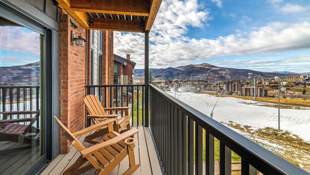 A balcony with wooden chairs, a brick wall, and a view of a cityscape and mountains. - Bear Claw 203 Premium On Mountain Condo With Ski-In/Ski-Out Access! (Steamboat Springs)