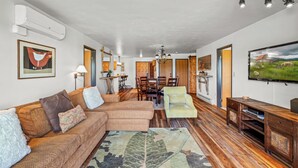 A spacious living room with a sectional sofa, a dining area, and a TV mounted on the wall. - Bear Claw 208 - Mountain Condo With Ski-In/Ski-Out Access! (Steamboat Springs)
