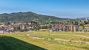 A residential area with multi-story buildings, a green field, and a mountain in the background. - Bear Claw 208 - Mountain Condo With Ski-In/Ski-Out Access! (Steamboat Springs)