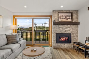 A living room with a fireplace, a sofa, a coffee table, and a view of the outdoors.