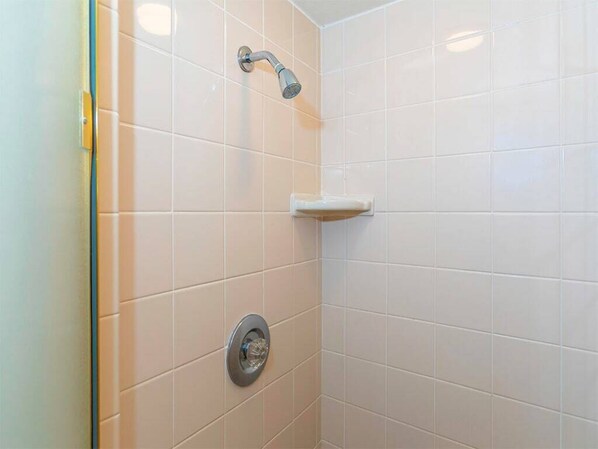 A bathroom with white tiles, a showerhead, and a toilet. - Easy-Going Style w/Lanai, Kitchen Ease, WiFi, Washer/Dryer–Kamaole Sands 5314 (KIHEI)