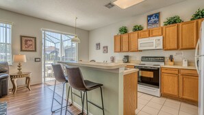 Una cocina moderna con armarios de madera, una isla central con taburetes altos, microondas, estufa y refrigerador.