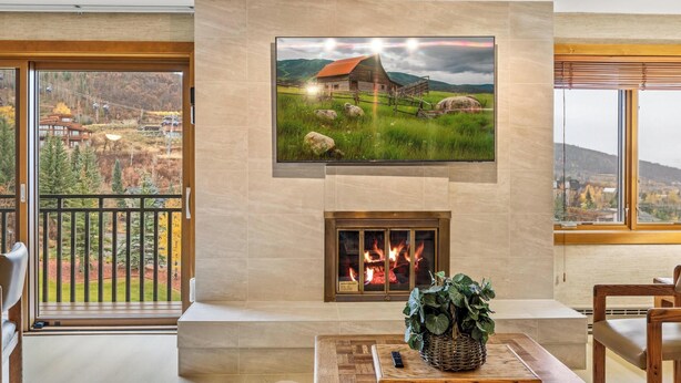 Una sala de estar moderna con chimenea, un televisor grande montado sobre ella y vistas a un paisaje montañoso a través de amplios ventanales.